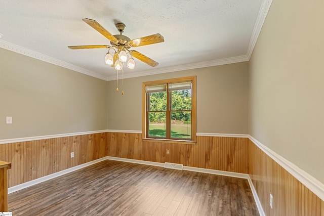 unfurnished room featuring crown molding, ceiling fan, a textured ceiling, dark hardwood / wood-style flooring, and wood walls