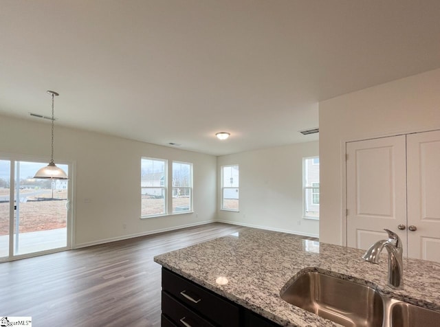 kitchen with pendant lighting, light stone counters, wood-type flooring, and sink