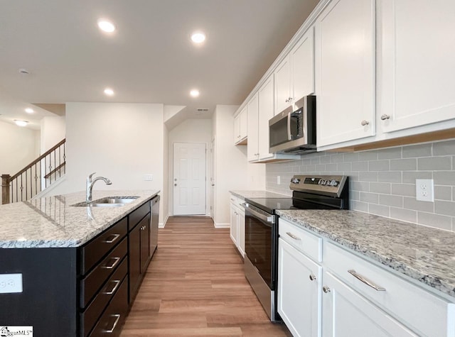 kitchen with stainless steel appliances, a kitchen island with sink, sink, white cabinets, and light hardwood / wood-style floors