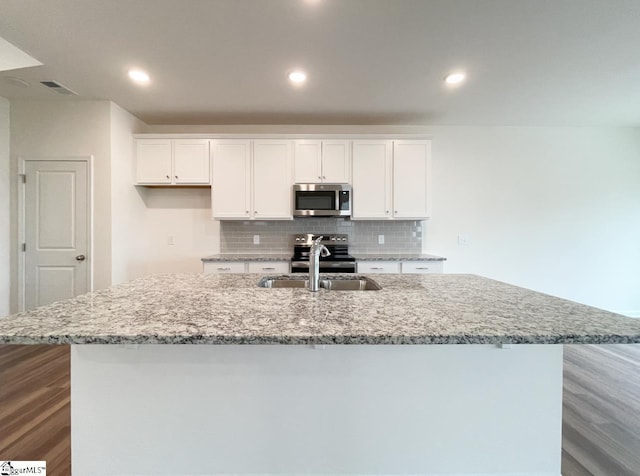 kitchen with stainless steel appliances, white cabinetry, a large island, and sink