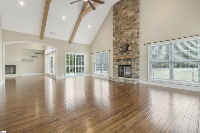 unfurnished living room featuring a stone fireplace, high vaulted ceiling, ceiling fan, beam ceiling, and hardwood / wood-style floors