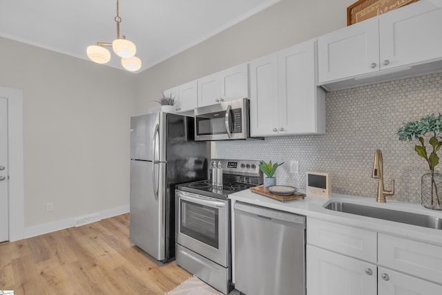 kitchen featuring decorative backsplash, white cabinets, appliances with stainless steel finishes, crown molding, and a sink