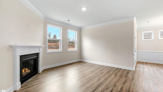 unfurnished living room with visible vents, ornamental molding, a glass covered fireplace, light wood-style floors, and baseboards