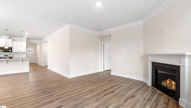 unfurnished living room featuring baseboards, wood finished floors, a glass covered fireplace, and crown molding