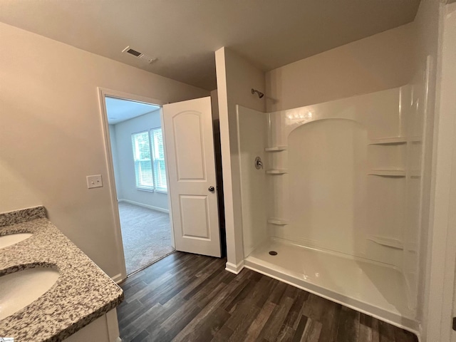 bathroom with a shower, dual vanity, and wood-type flooring