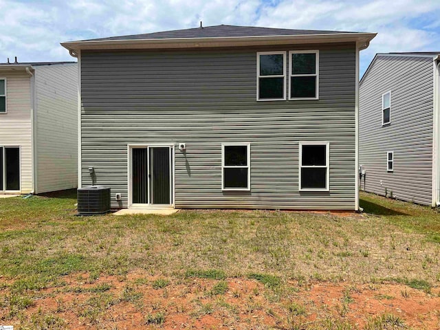 rear view of property with central air condition unit and a lawn