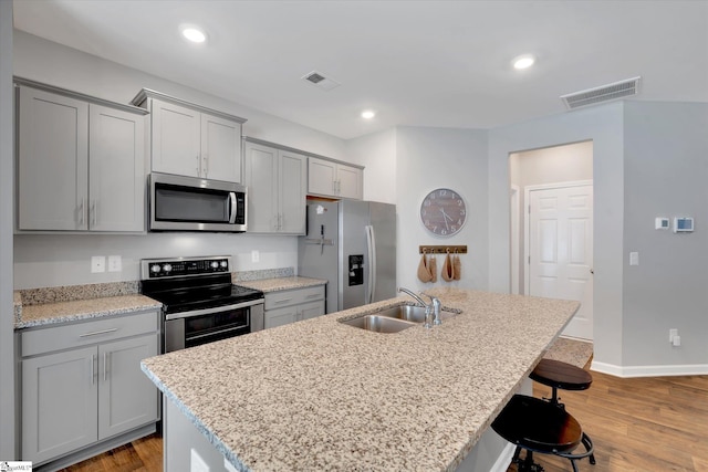 kitchen with sink, a kitchen breakfast bar, an island with sink, stainless steel appliances, and light stone countertops