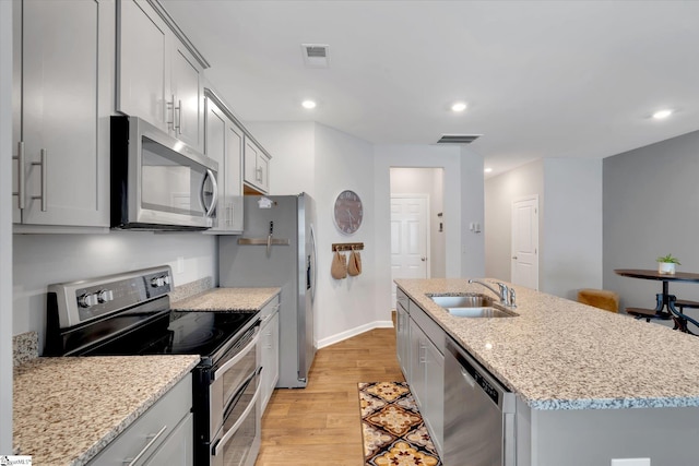 kitchen with an island with sink, stainless steel appliances, light stone countertops, and sink