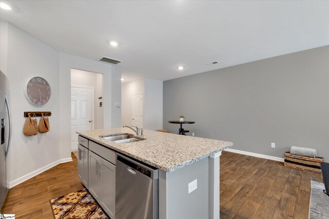 kitchen featuring appliances with stainless steel finishes, sink, light stone counters, light wood-type flooring, and an island with sink