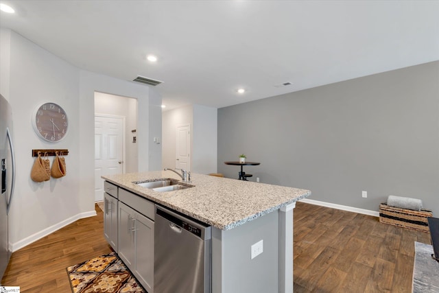 kitchen featuring appliances with stainless steel finishes, sink, light stone counters, an island with sink, and dark hardwood / wood-style flooring