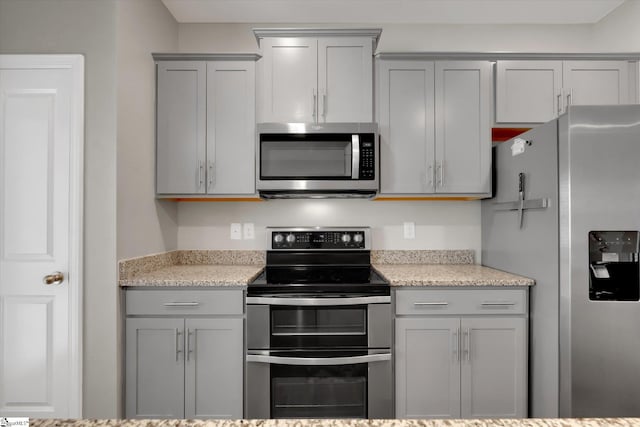 kitchen featuring light stone counters, stainless steel appliances, and gray cabinetry