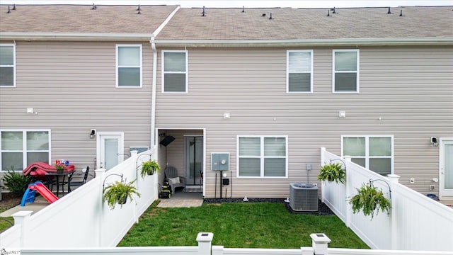 rear view of house featuring central air condition unit and a lawn