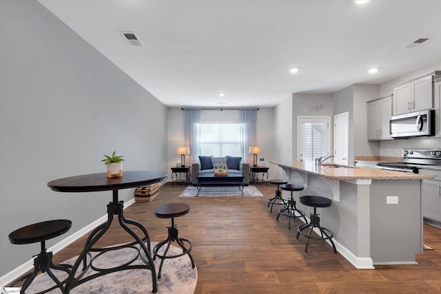 kitchen with a center island with sink, dark hardwood / wood-style flooring, a kitchen breakfast bar, stainless steel appliances, and light stone countertops