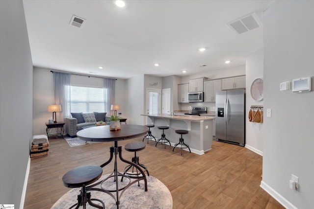 kitchen featuring a breakfast bar area, gray cabinetry, a kitchen island with sink, light hardwood / wood-style floors, and stainless steel appliances