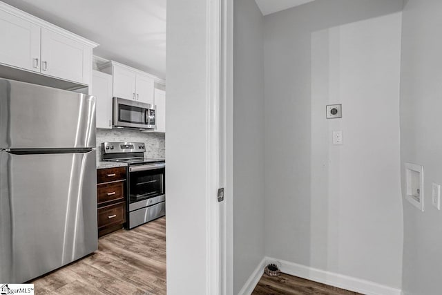 kitchen with light wood-type flooring, stainless steel appliances, white cabinetry, and tasteful backsplash