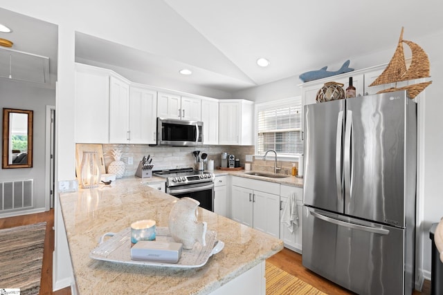 kitchen featuring white cabinetry, stainless steel appliances, vaulted ceiling, light stone counters, and sink