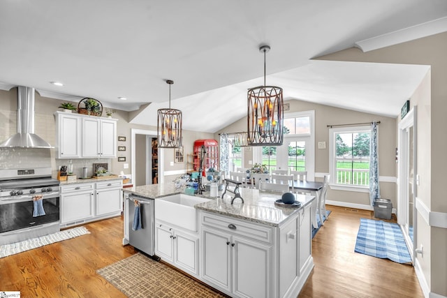 kitchen featuring wall chimney exhaust hood, white cabinetry, a center island with sink, appliances with stainless steel finishes, and light hardwood / wood-style floors