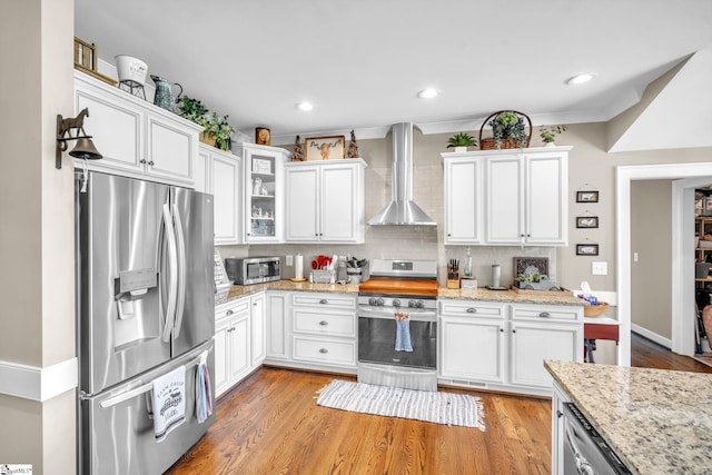 kitchen featuring wall chimney range hood, light hardwood / wood-style flooring, appliances with stainless steel finishes, white cabinetry, and tasteful backsplash