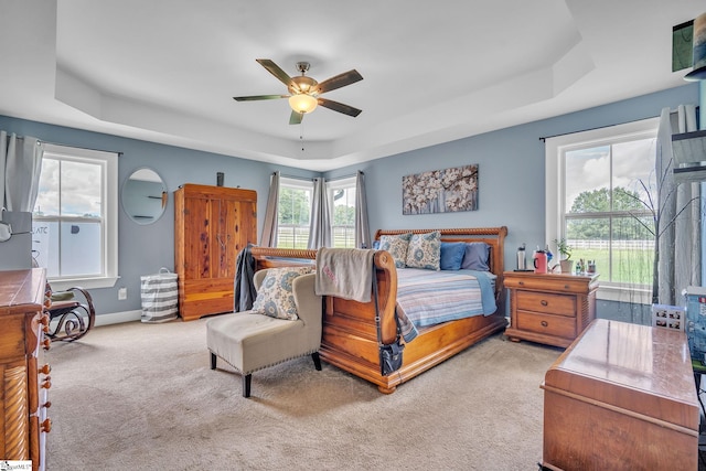 bedroom featuring a raised ceiling, light colored carpet, and ceiling fan