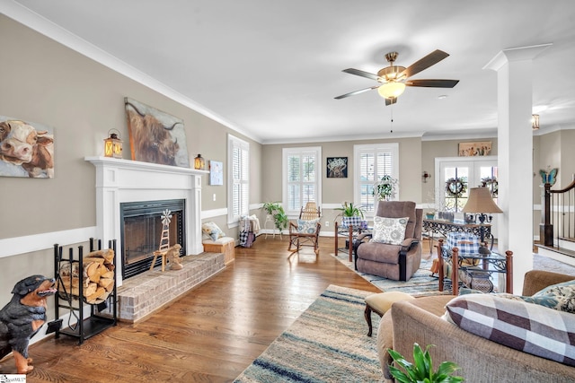 living room featuring a brick fireplace, hardwood / wood-style flooring, ornamental molding, and ceiling fan