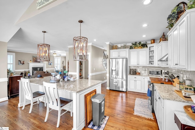 kitchen featuring a breakfast bar area, appliances with stainless steel finishes, white cabinetry, a kitchen island, and decorative light fixtures