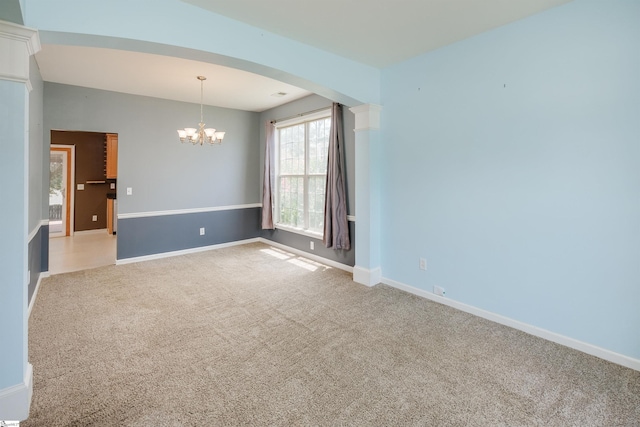 carpeted spare room featuring an inviting chandelier and ornate columns