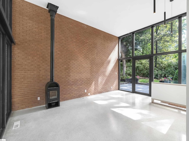 empty room featuring visible vents, a high ceiling, a wood stove, brick wall, and a wall of windows