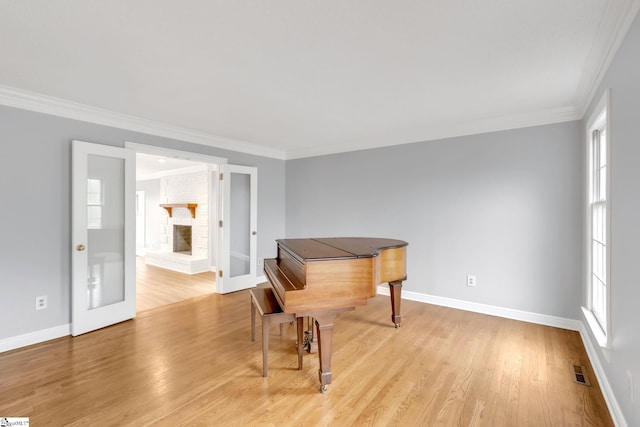 sitting room with light wood-type flooring, visible vents, crown molding, baseboards, and a brick fireplace