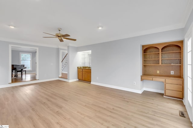 unfurnished living room with visible vents, built in desk, light wood finished floors, and baseboards