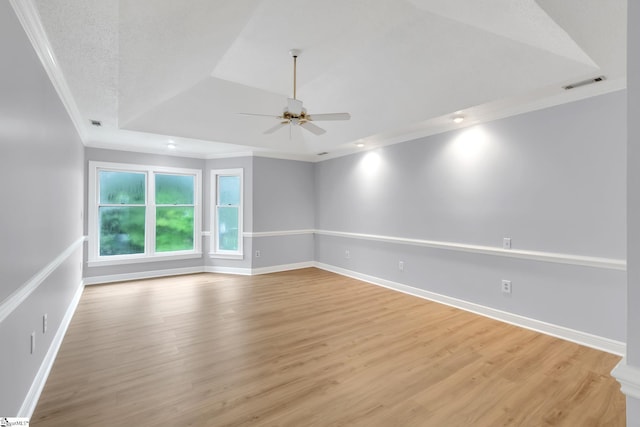 spare room with light wood-type flooring, visible vents, ornamental molding, baseboards, and a raised ceiling