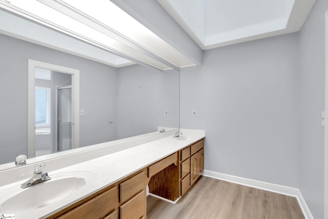 full bathroom featuring a sink, wood finished floors, a shower stall, double vanity, and baseboards