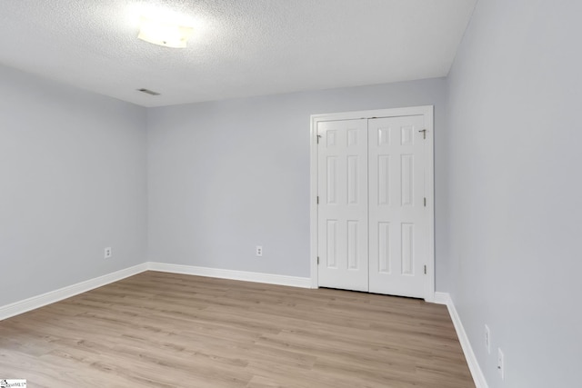 unfurnished bedroom featuring a closet, a textured ceiling, baseboards, and light wood-style floors