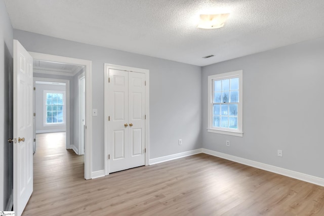 unfurnished bedroom with visible vents, a textured ceiling, a closet, light wood finished floors, and baseboards