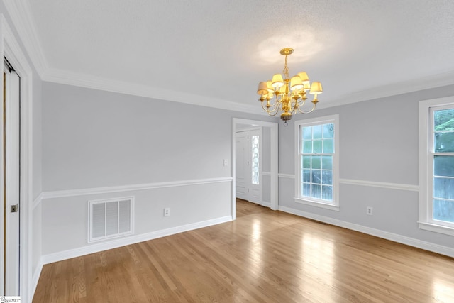 empty room featuring a notable chandelier, visible vents, ornamental molding, and wood finished floors