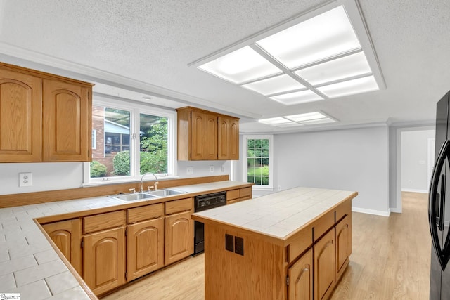 kitchen with tile counters, light wood-style flooring, black appliances, and a sink