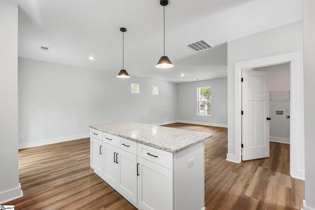 kitchen with pendant lighting, light stone counters, a center island, white cabinetry, and hardwood / wood-style flooring