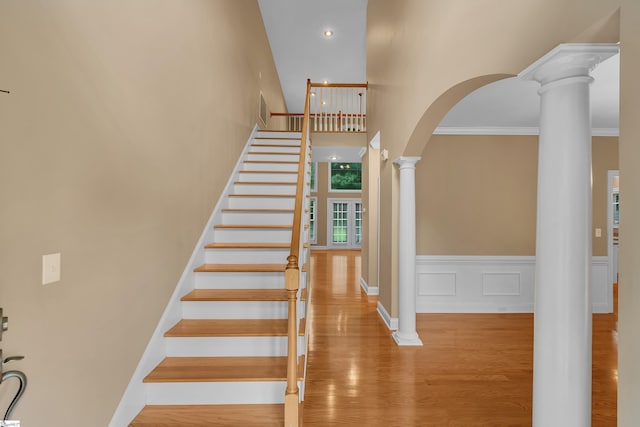 stairway with arched walkways, wood finished floors, ornamental molding, wainscoting, and ornate columns