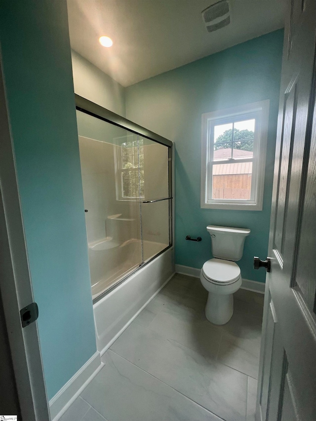 bathroom with toilet, tile patterned floors, and bath / shower combo with glass door