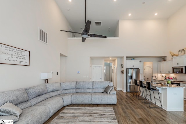 living room with a ceiling fan, a high ceiling, visible vents, and wood finished floors