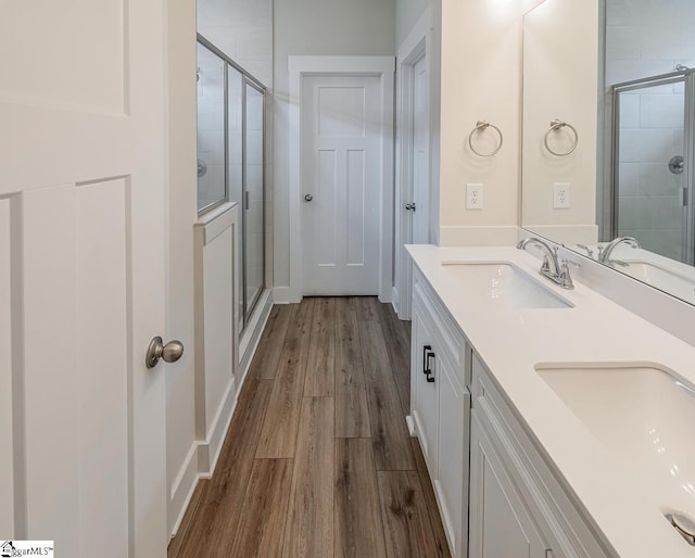 bathroom with double vanity, wood finished floors, a stall shower, and a sink