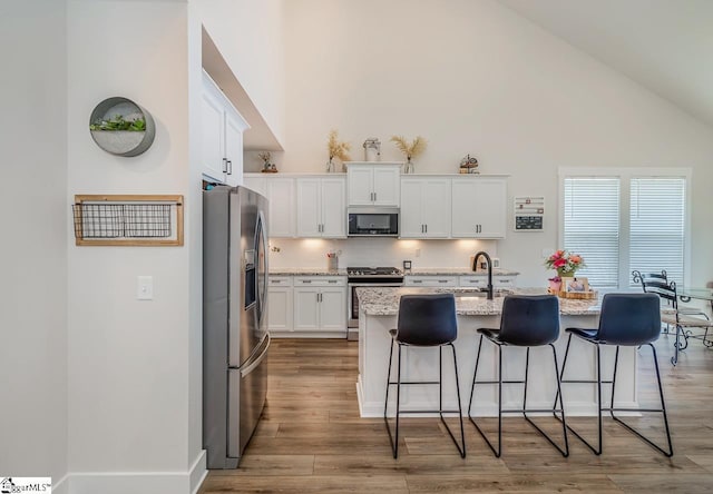 kitchen featuring stainless steel appliances, light stone counters, an island with sink, and white cabinetry