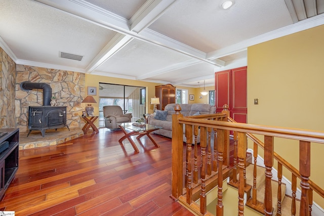 living area with wood finished floors, visible vents, beam ceiling, a wood stove, and crown molding