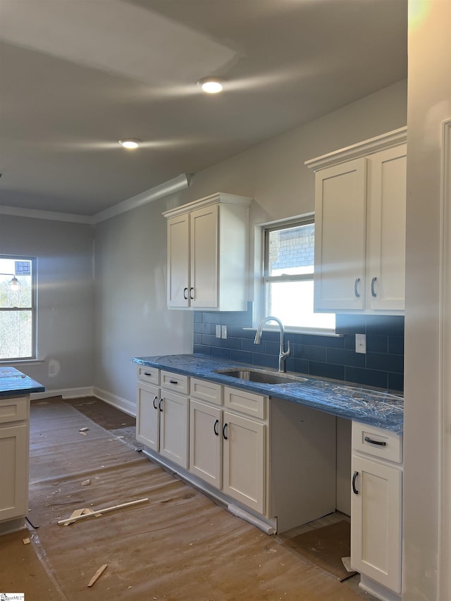 kitchen featuring baseboards, white cabinets, wood finished floors, a sink, and backsplash