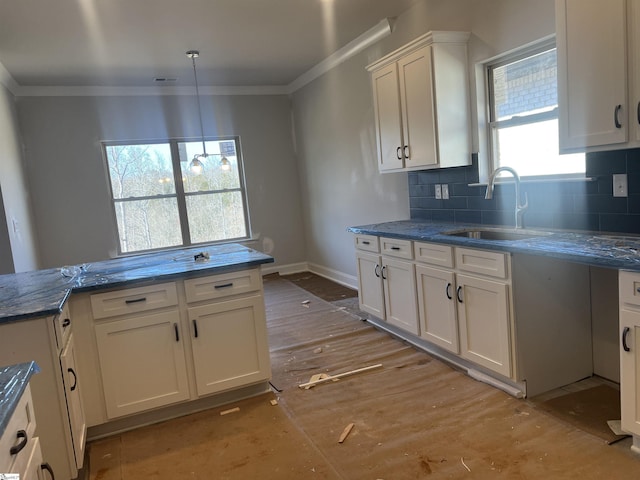 kitchen with crown molding, white cabinets, a sink, and backsplash