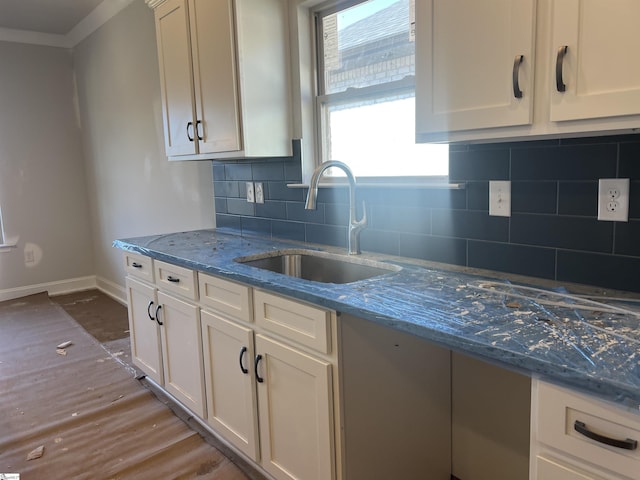 kitchen featuring stone counters, a sink, white cabinets, baseboards, and decorative backsplash