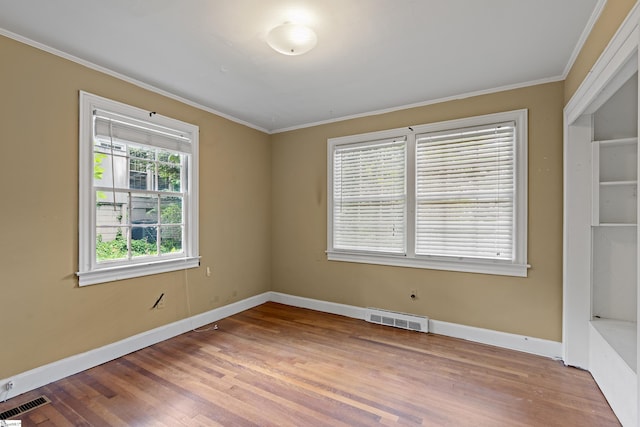 empty room with baseboards, crown molding, visible vents, and wood finished floors