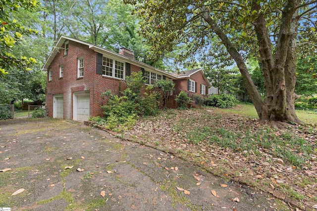 view of front of property featuring driveway, brick siding, a chimney, and an attached garage