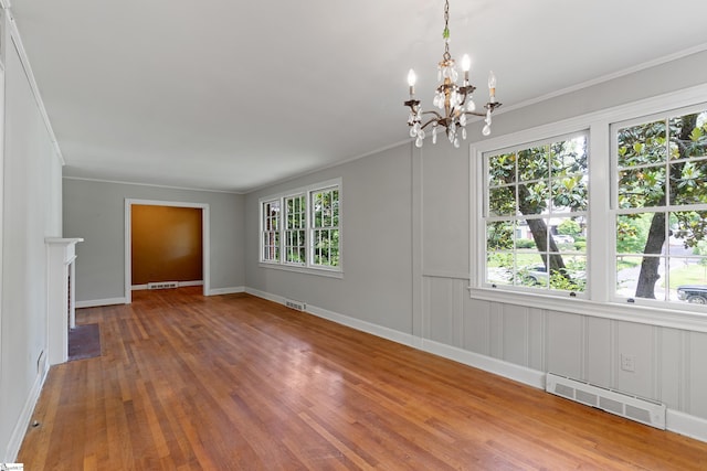 empty room with a notable chandelier, visible vents, wood finished floors, and ornamental molding