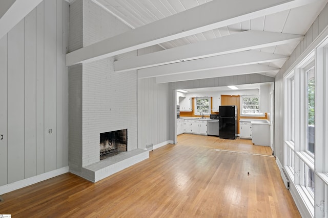 unfurnished living room featuring a brick fireplace, baseboards, vaulted ceiling with beams, and light wood finished floors