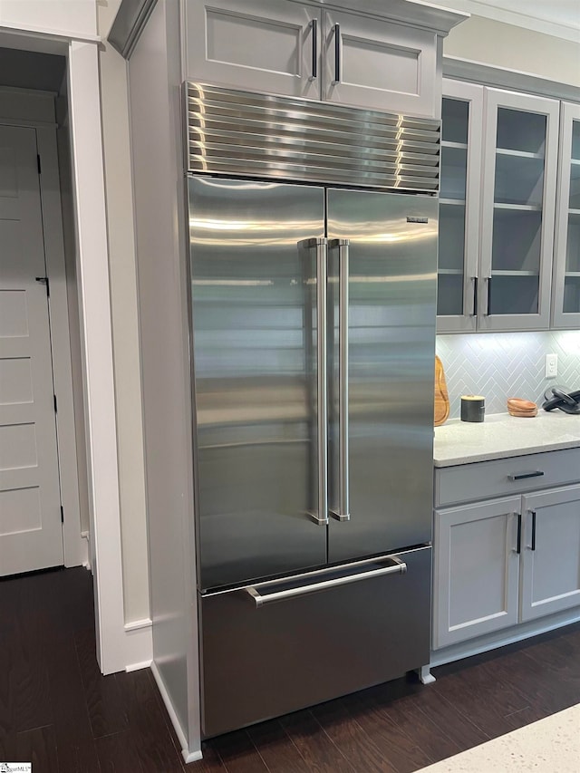 kitchen with light stone counters, backsplash, dark wood-type flooring, and built in refrigerator